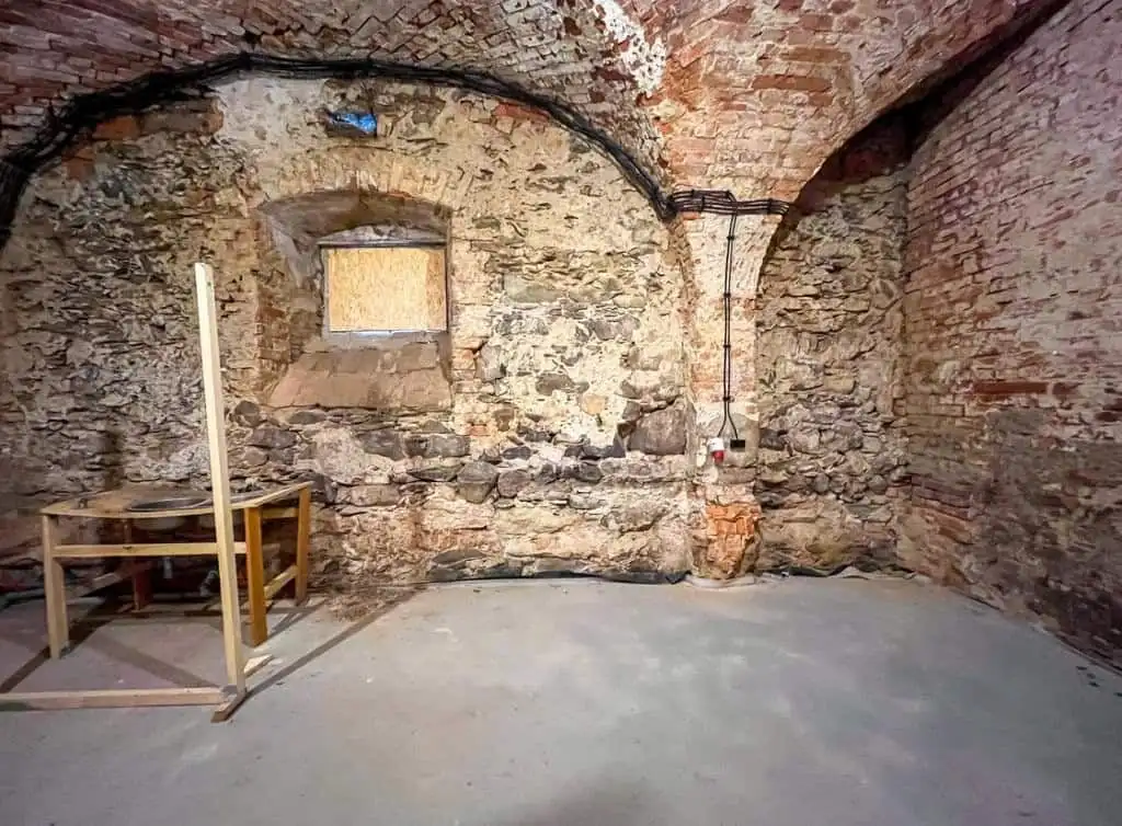 Ancient stone cellar with brick arches, small window, and unfinished floor.