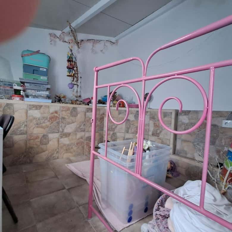 Beautiful pink metal bed frame in a cozy, rustic room with stone walls and storage shelves.