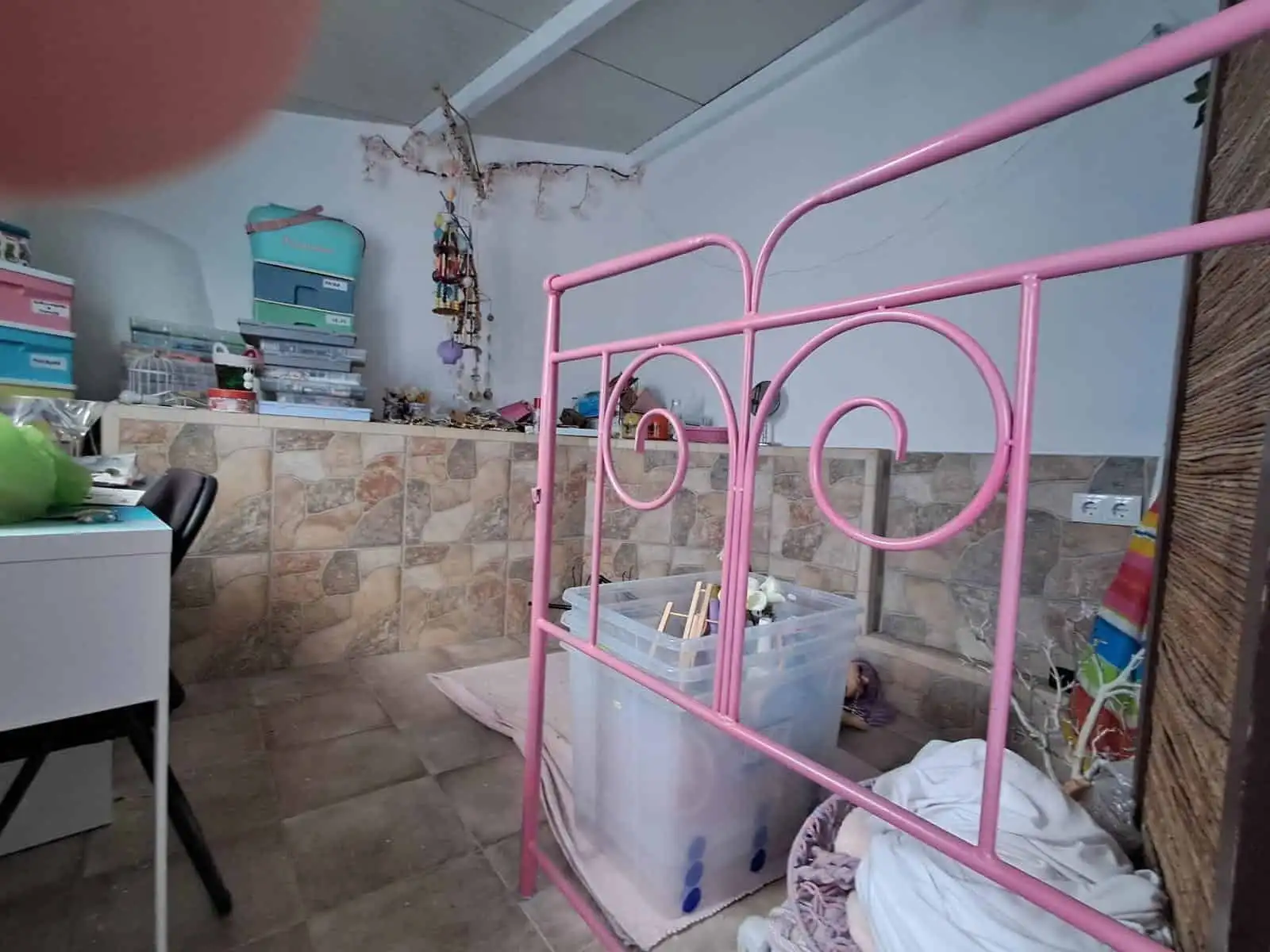 Beautiful pink metal bed frame in a cozy, rustic room with stone walls and storage shelves.