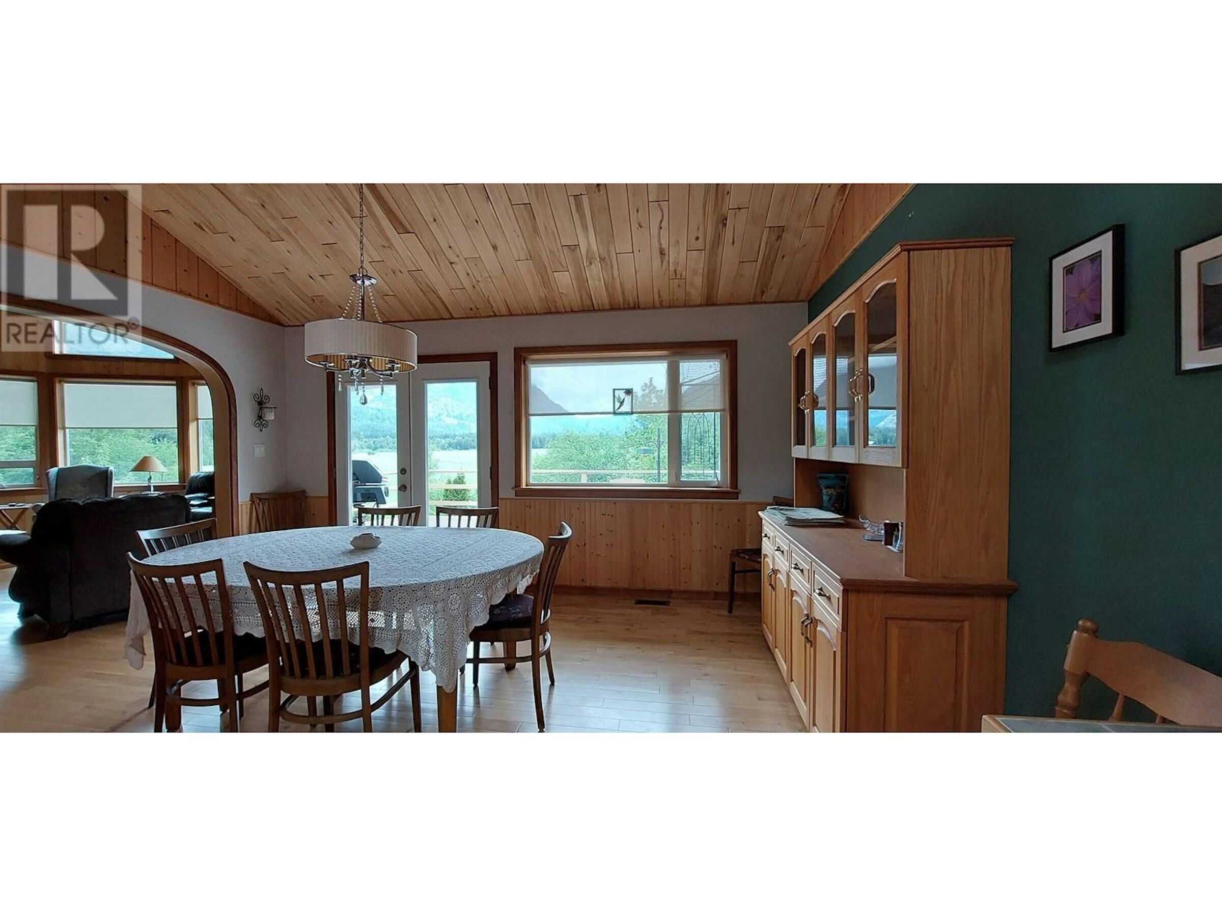 Spacious dining room with wooden ceiling and large windows offering scenic views in Bella Coola esta.