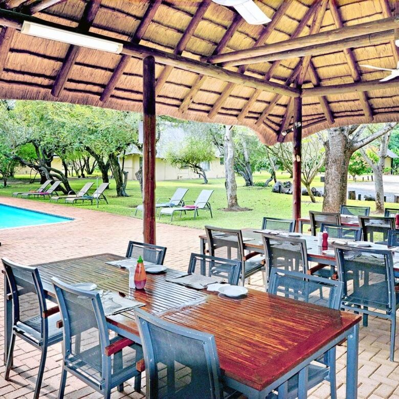 Outdoor dining area at Komati River Chalets with pool and lush garden views.