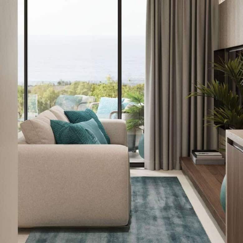 Modern Bali apartment living room with sea view, featuring a cozy sofa, large windows, and lush gree.