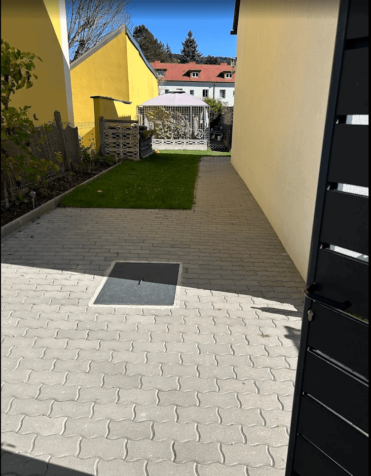 Modern building with 4 apartments for sale in Wilhelmsburg, featuring a paved driveway and garden area. Building with 4 Apartments for Sale in Wilhelmsburg, showing exterior view and outdoor space.