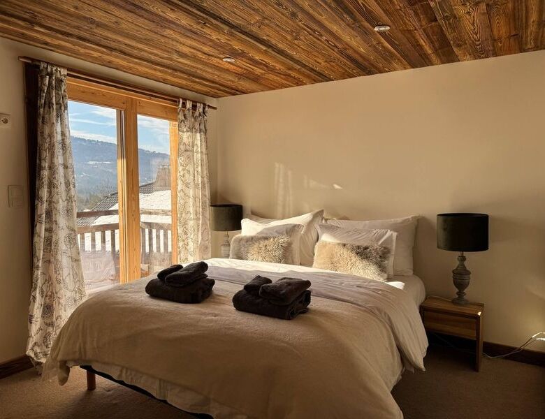 Cozy bedroom in a luxury chalet with wooden ceiling and large windows overlooking scenic mountain vi.