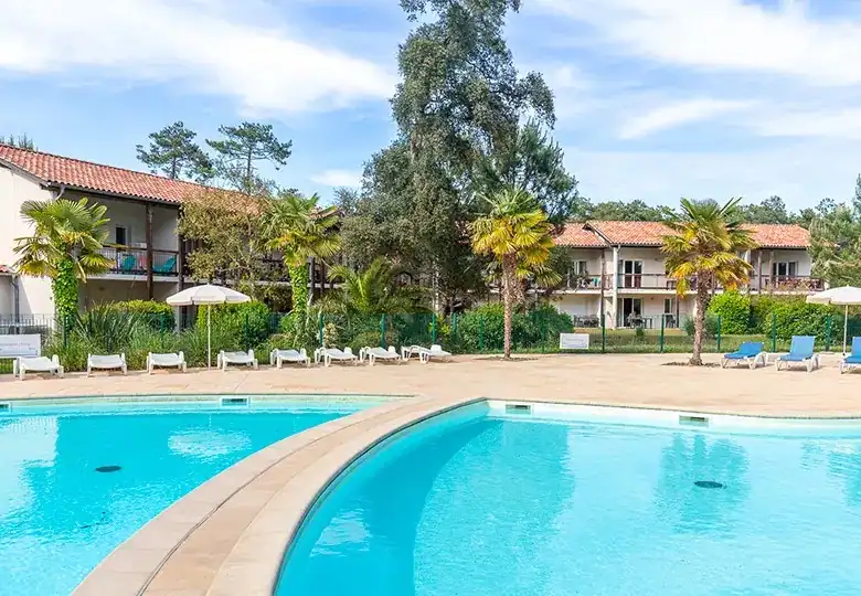 Pool area with lounge chairs, umbrellas, and lush greenery.