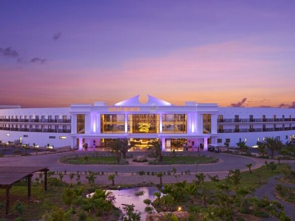 Modern hotel at sunset with vibrant lighting and lush gardens.
