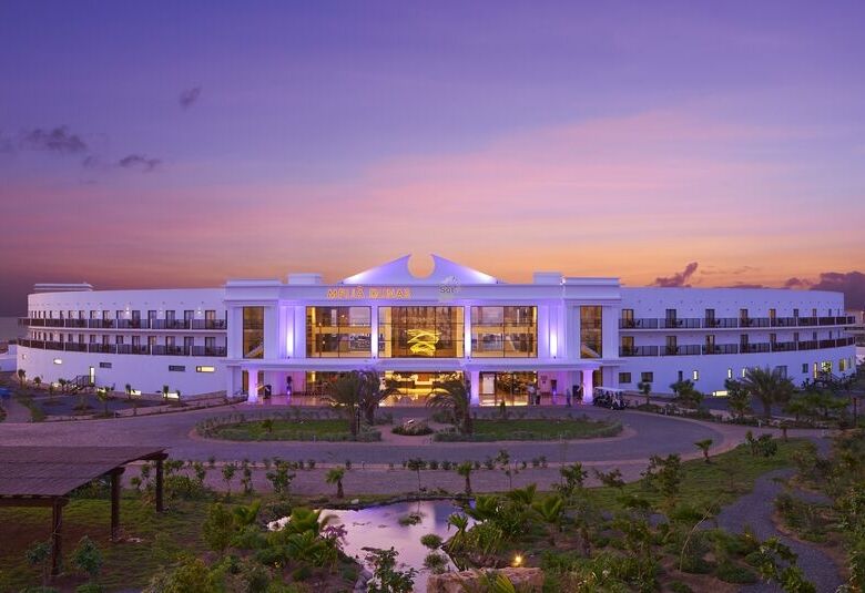 Modern hotel at sunset with vibrant lighting and lush gardens.