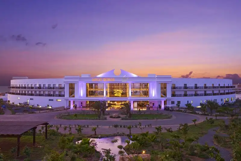 Modern hotel at sunset with vibrant lighting and lush gardens.