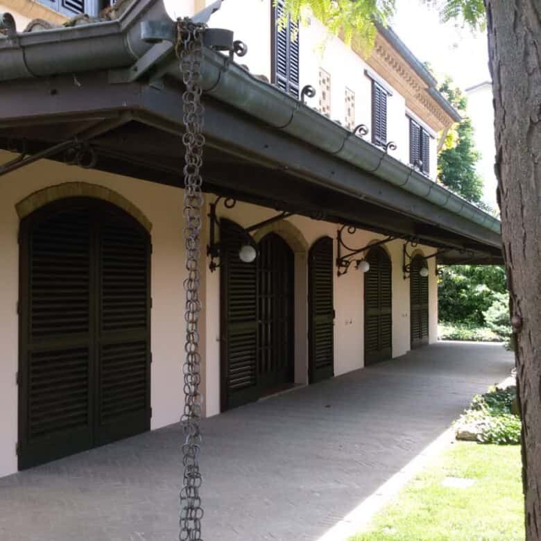 Elegant estate with shaded porch, lush greenery, and vibrant flowers in Forli.