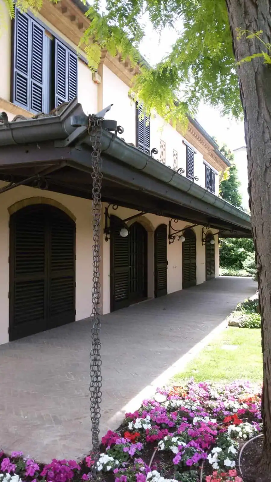 Elegant estate with shaded porch, lush greenery, and vibrant flowers in Forli.