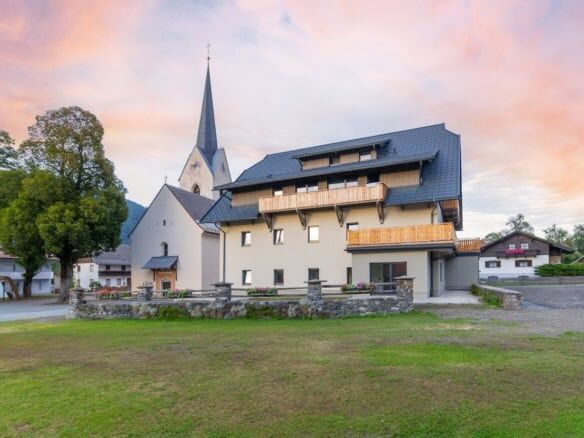 Modern apartment building near a church in Rattendorf at sunset.