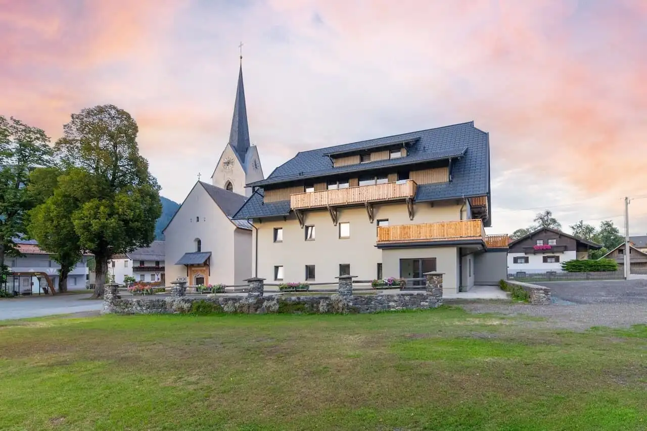 Modern apartment building near a church in Rattendorf at sunset.