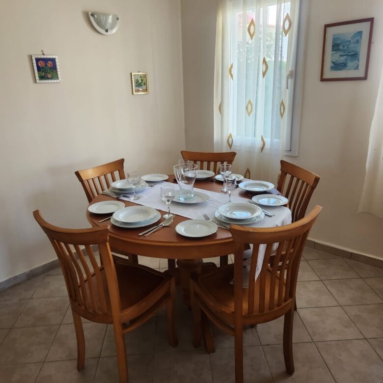 Elegant dining room with wooden table and six chairs, bright natural light, and seaside artwork.