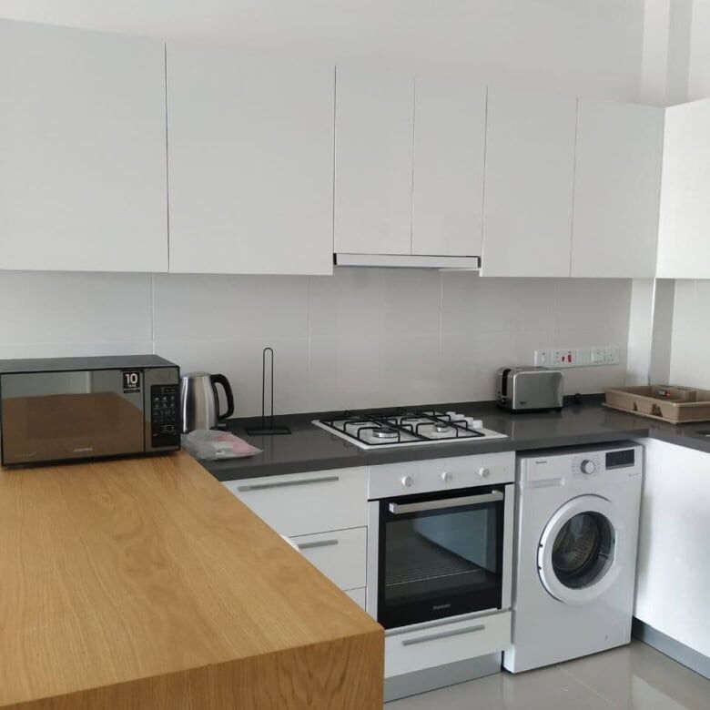 Modern kitchen with white cabinets, oven, washing machine, microwave, and countertop in Caeser’s Res.