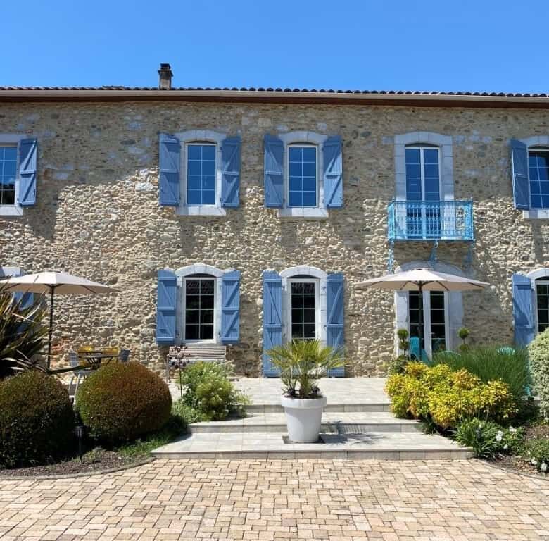 Built bed and breakfast with blue shutters, lush garden, and outdoor seating in Ausson, Haute Garonn.