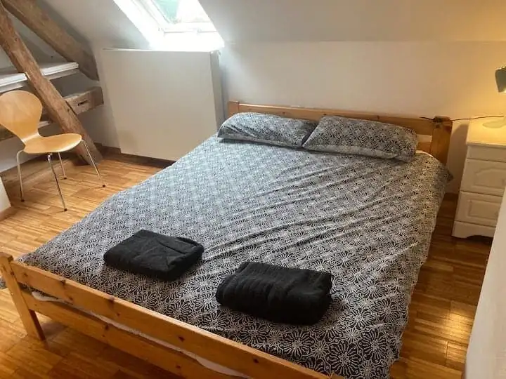 Comfortable bedroom featuring a wooden bed frame, two folded towels, and ample natural light from a.