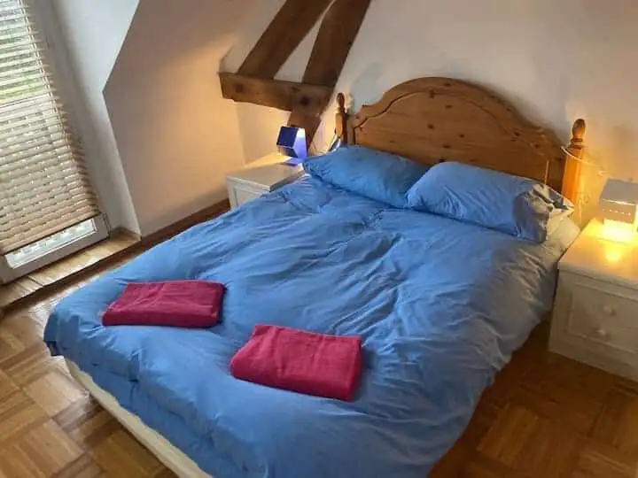 Bright bedroom featuring a wooden bed frame, blue bedding, and natural light from a nearby window.