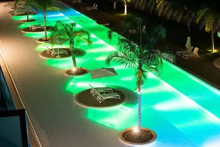 Beautiful illuminated pool with palm trees and lounge chairs at night in Punta Cana.