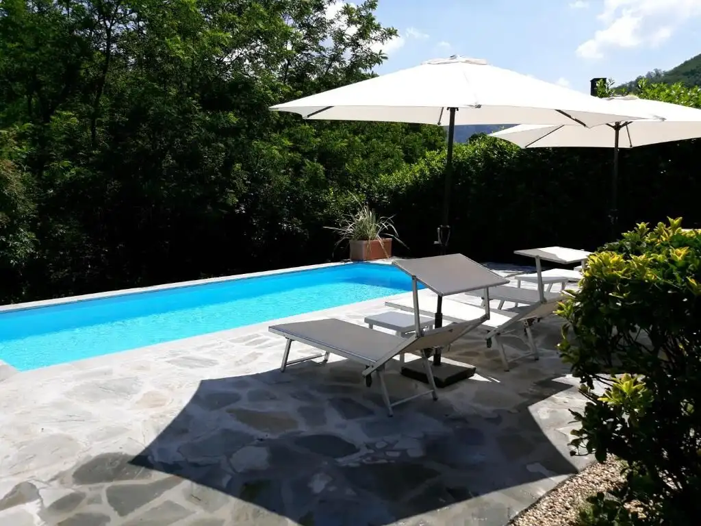 Elegant outdoor pool with sun loungers and umbrellas in scenic countryside setting.