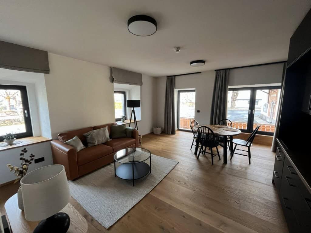 Modern living room with large windows and stylish furniture in Rattendorf. Spacious apartment interior with comfortable seating, dining area, and natural light.