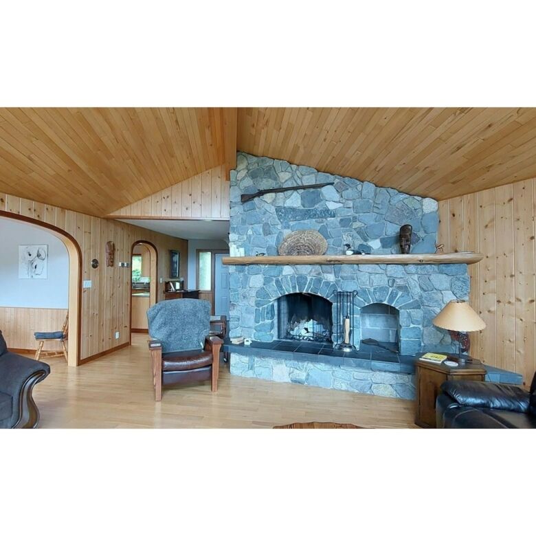 Spacious living room with a stone fireplace and wooden accents in this beautiful estate for sale in.