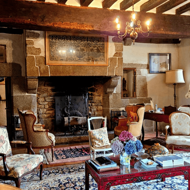 Charming interior of a luxury Normandy home featuring a cozy stone fireplace and antique furnishings.