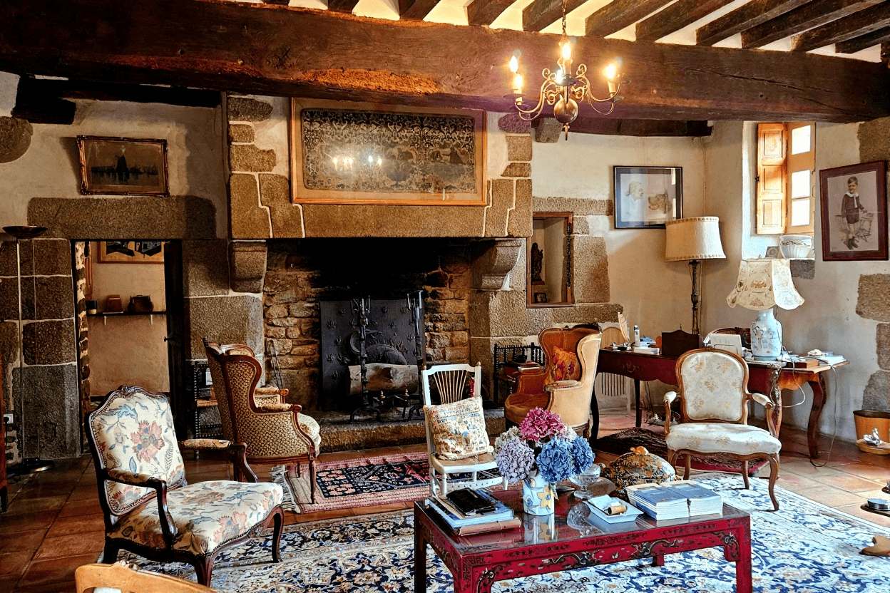 Elegant living room with rustic stone fireplace and vintage furniture. Charming interior of a luxury Normandy home featuring a cozy stone fireplace and antique furnishings.