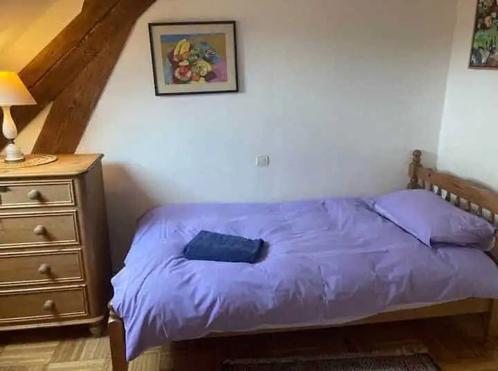 Cozy bedroom featuring a wooden bed frame, purple bedding, and decorative artwork on the wall.