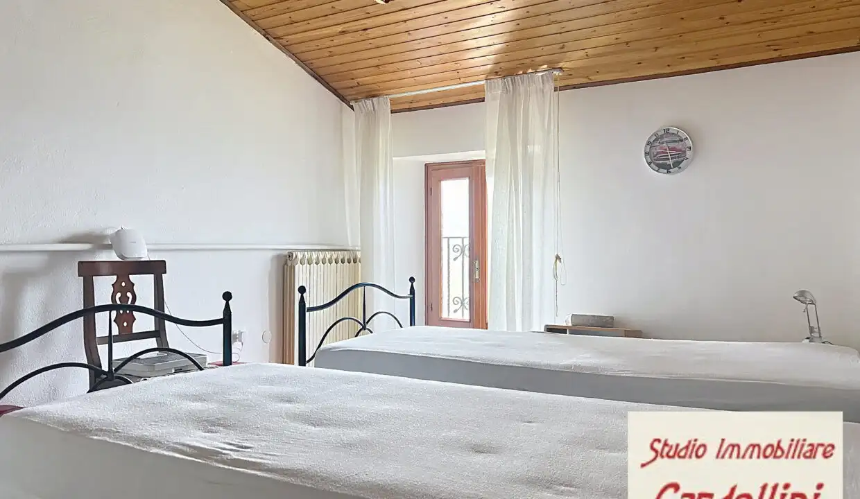 Spacious bedroom in Fivizzano, Tuscany, featuring two single beds, wooden ceiling, and natural light.