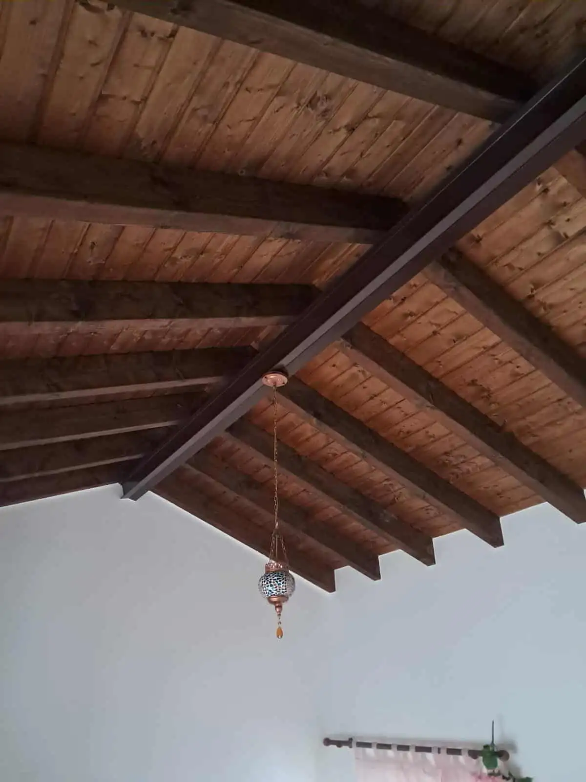 Wooden ceiling with beams and a hanging decorative lamp in a villa.