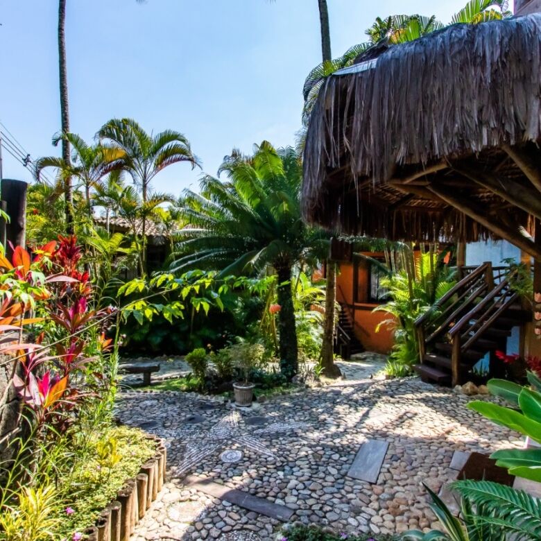 Boutique hotel for sale in Ilhabela featuring tropical gardens and traditional thatched roof structu.
