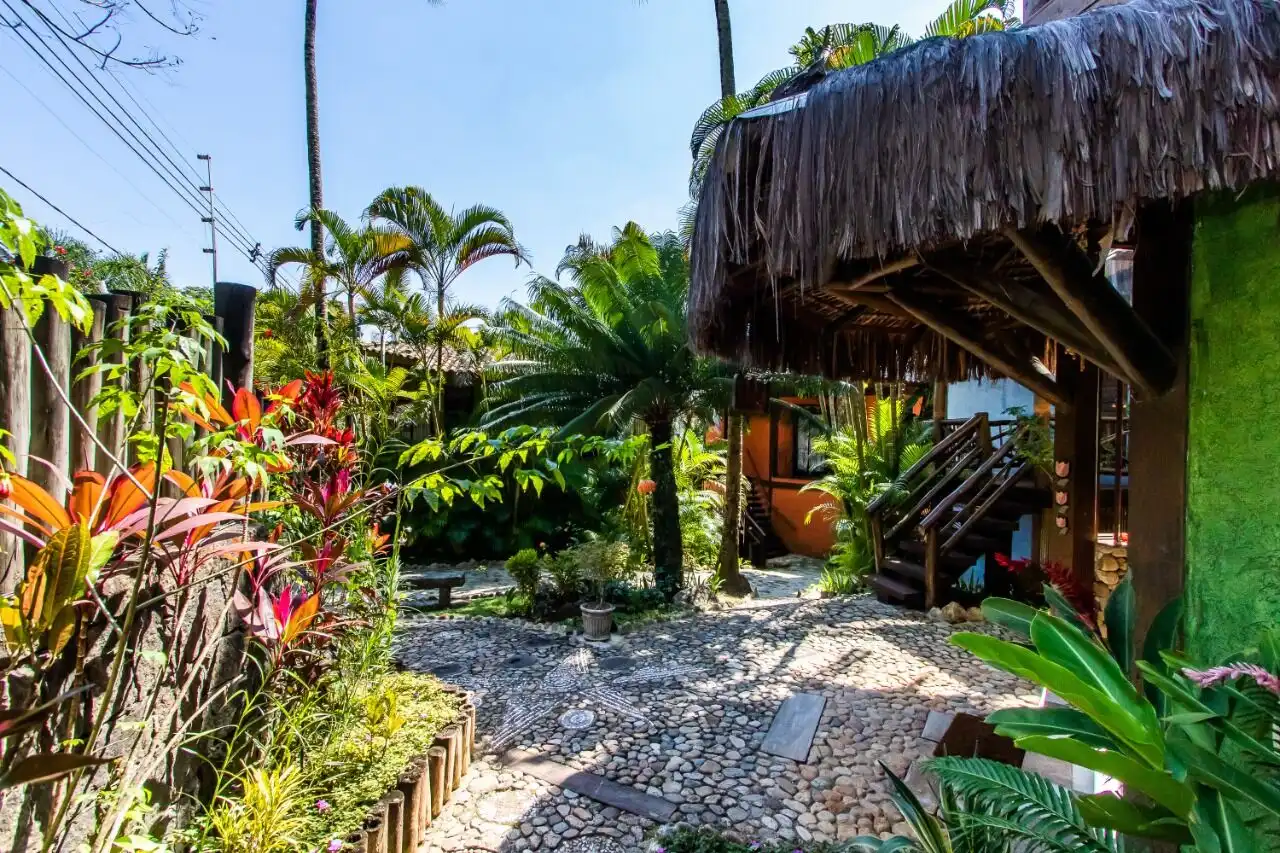 Boutique hotel for sale in Ilhabela featuring tropical gardens and traditional thatched roof structu.