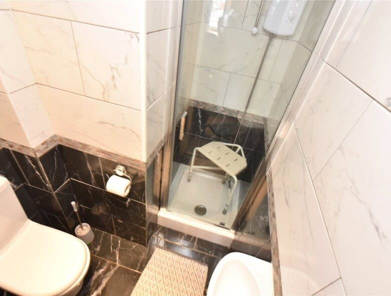 Small bathroom with shower, toilet, and tiled walls in Leeds property listing.