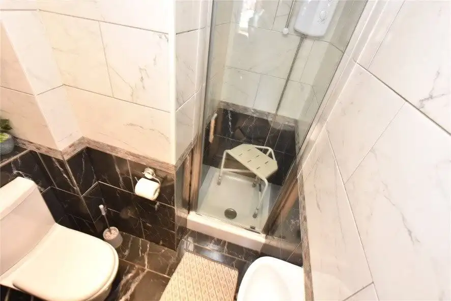 Small bathroom with shower, toilet, and tiled walls in Leeds property listing.