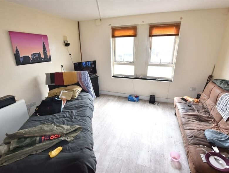 Apartment interior with two sofas, windows, and personal belongings.