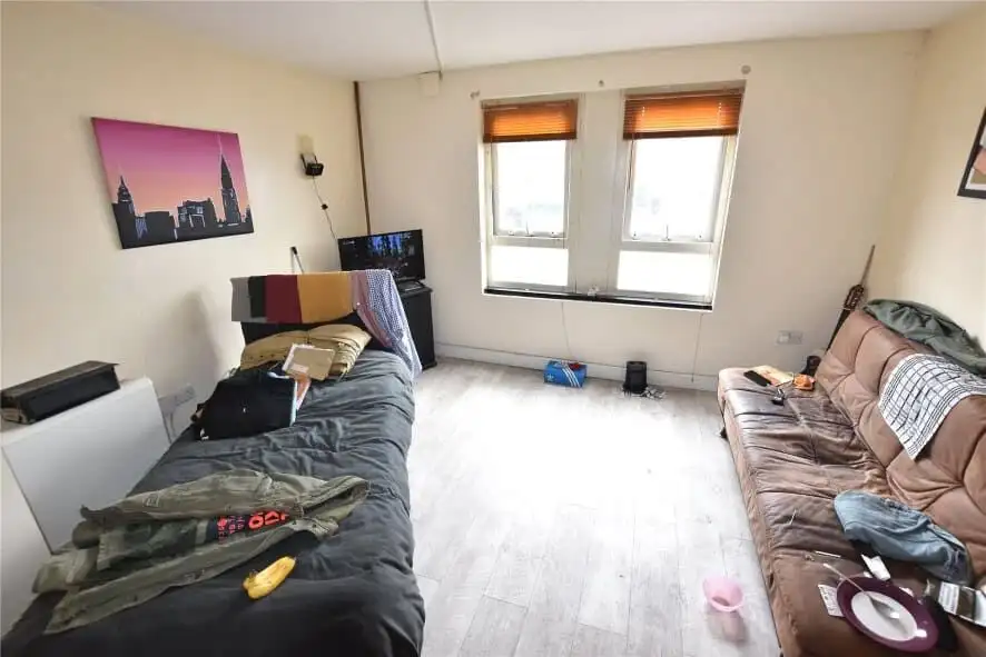Apartment interior with two sofas, windows, and personal belongings.