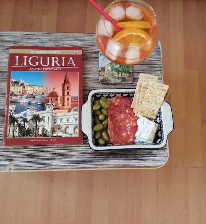 Tasty snack with wine, cheese, and crackers beside a Liguria travel book.