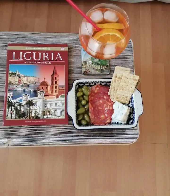 Tasty snack with wine, cheese, and crackers beside a Liguria travel book.