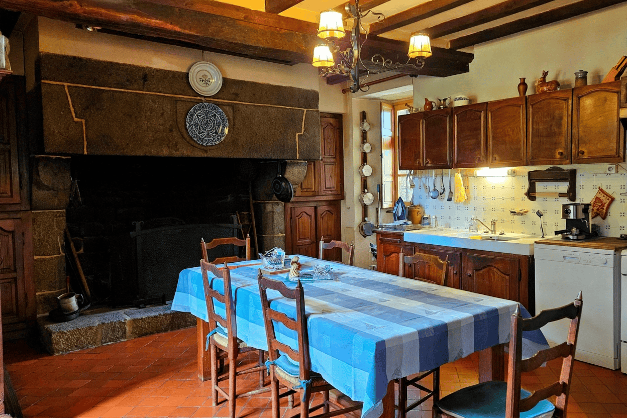 Charming Normandy Kitchen with Fireplace Cozy Normandy kitchen featuring a large fireplace, wooden cabinets, and a dining table with blue che.