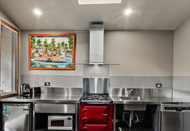 Modern kitchen featuring stainless steel appliances, a red oven, and ample natural light. Perfect fo.