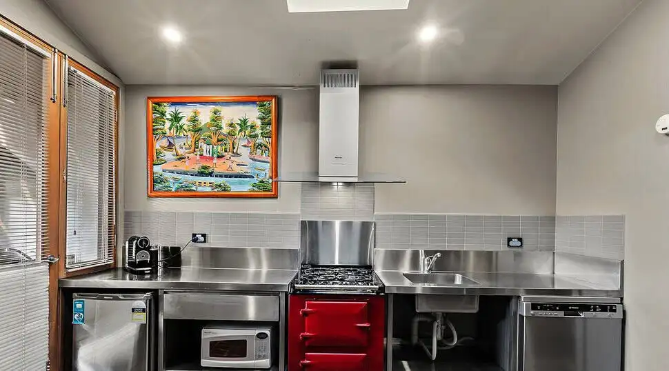 Modern kitchen featuring stainless steel appliances, a red oven, and ample natural light. Perfect fo.