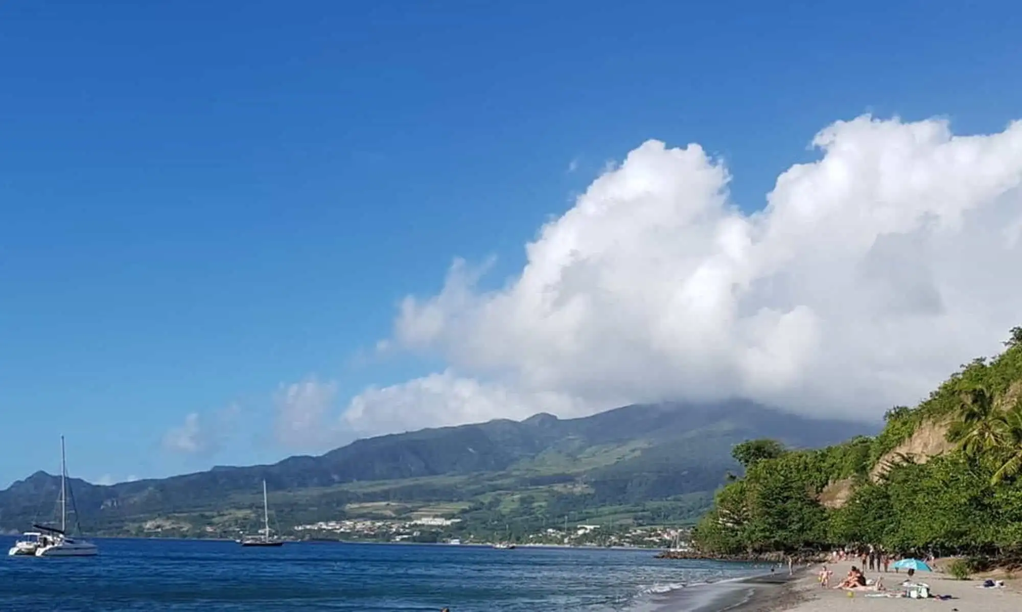 Scenic beach on Martinique island with clear waters and green hills in the background.