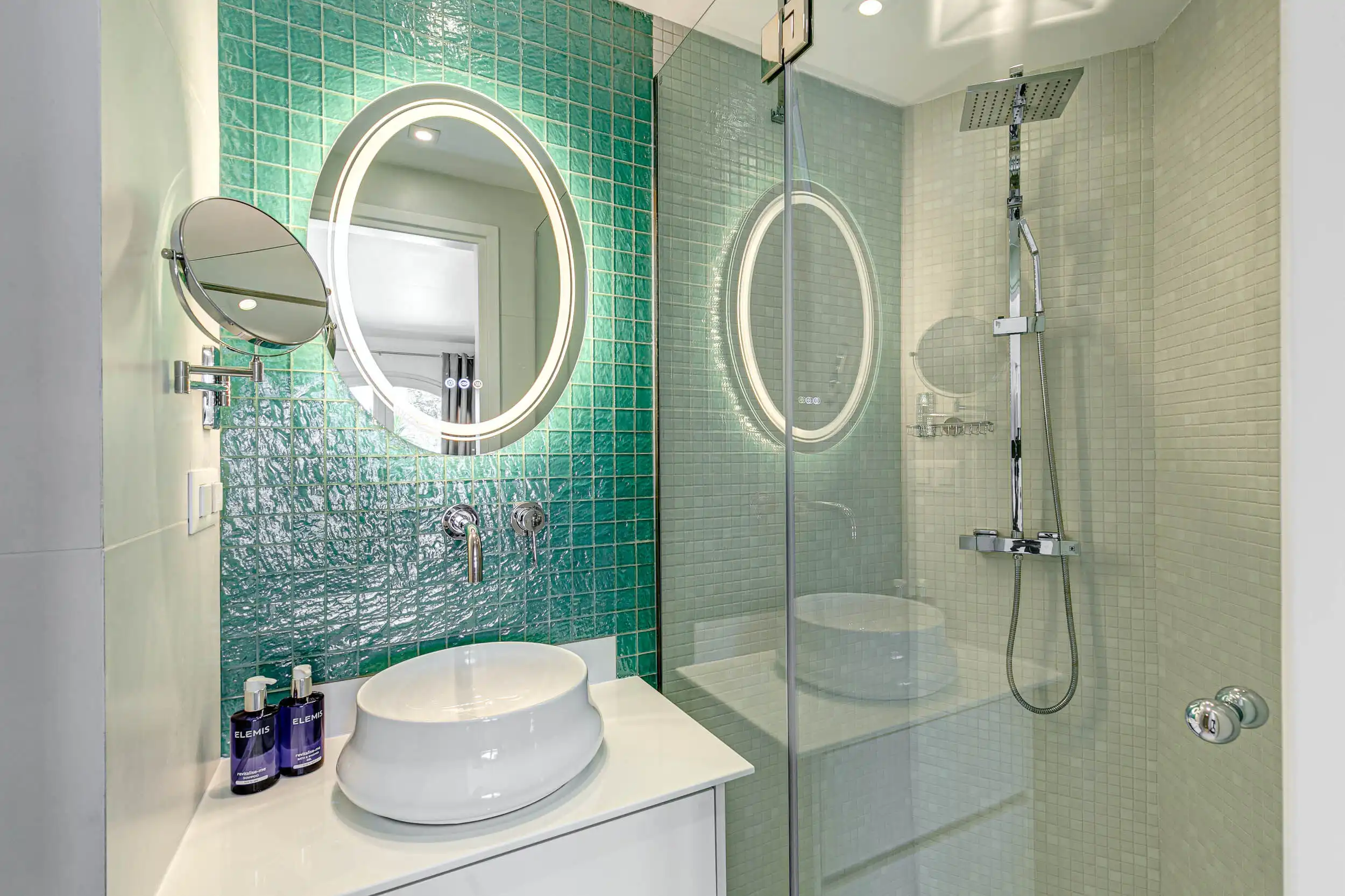 Luxury Villa Bathroom with Modern Fixtures Modern bathroom with green tiled wall, circular mirror, and glass shower enclosure in a luxury villa.