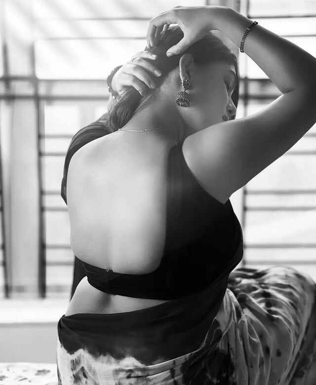 Elegant woman fixing hair, showcasing her back and earrings in a black dress.