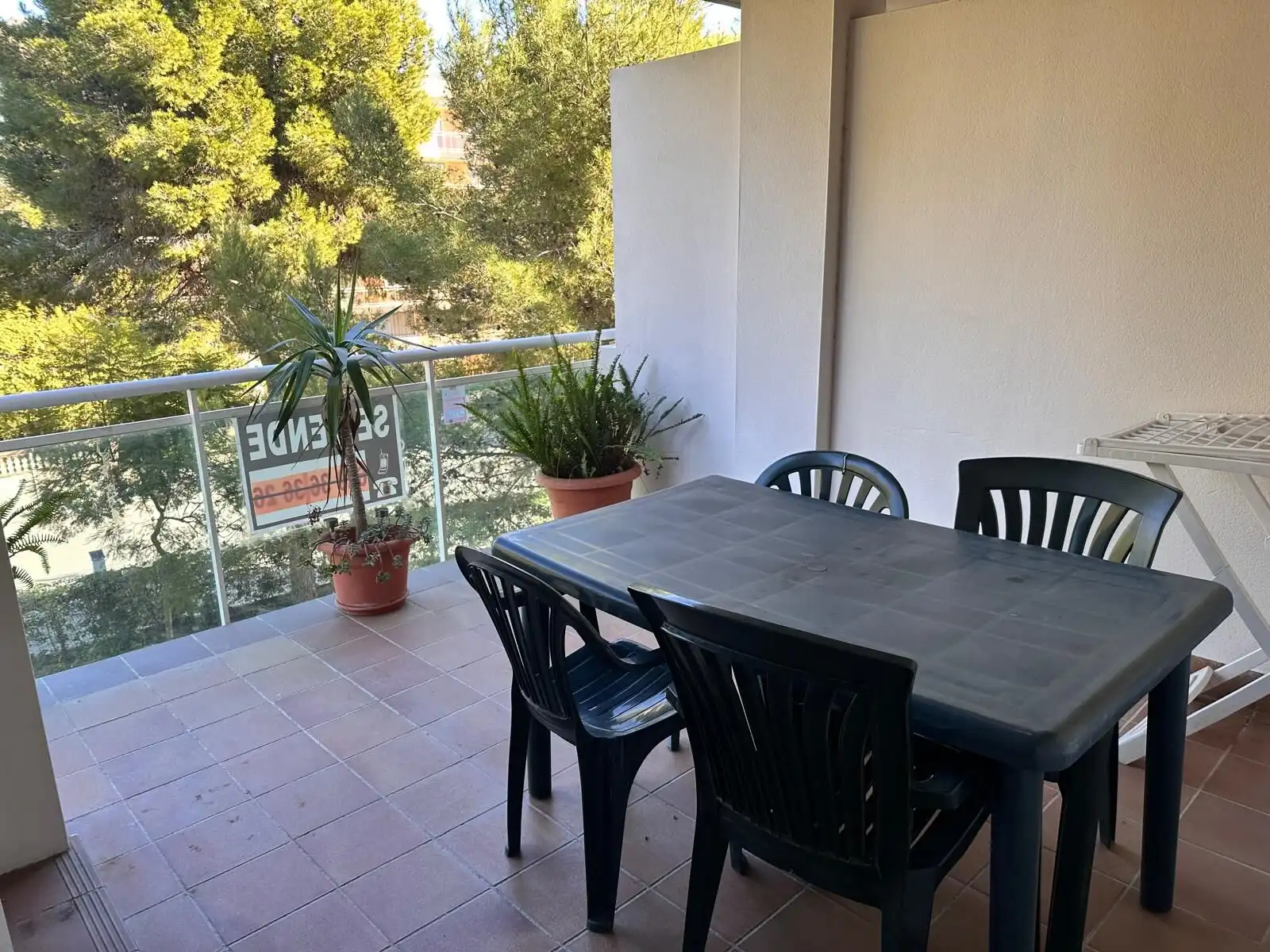 Balcony with a table and chairs, overlooking lush trees and a glass railing, perfect for relaxing ou.