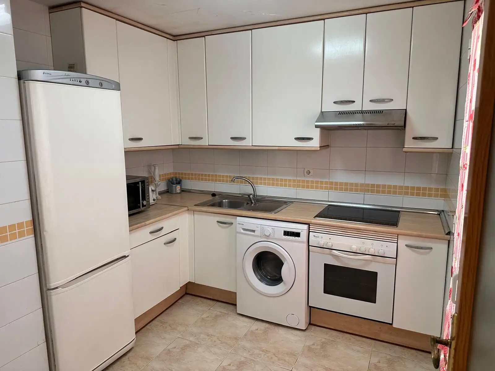 Modern kitchen with refrigerator, washing machine, oven, and microwave.