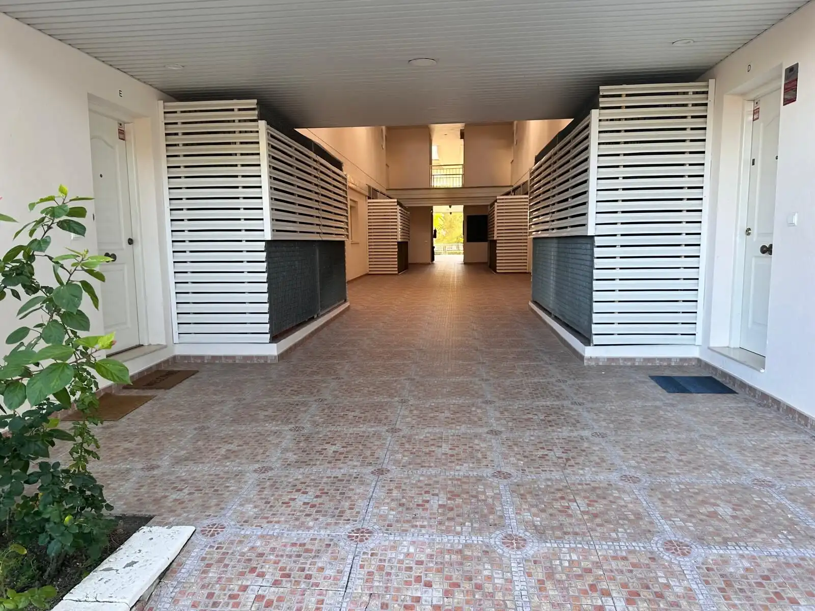 Modern apartment building entrance with private patios and white wooden fencing.