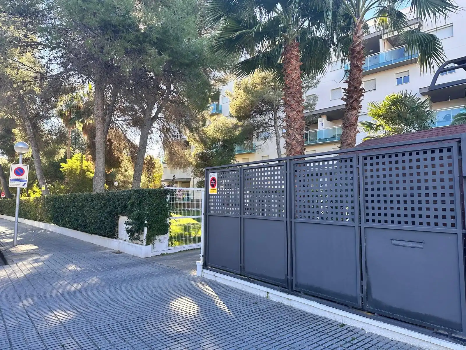 Gated entrance to a tourist apartment complex with palm trees and greenery.
