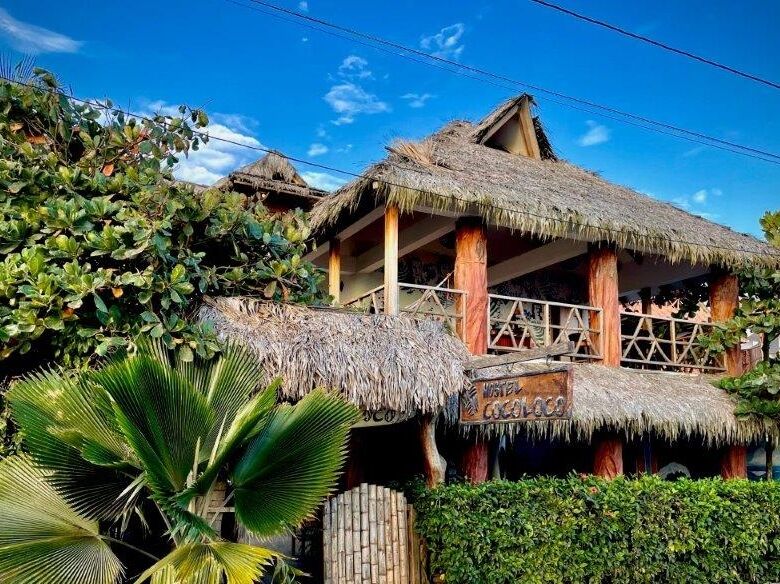 Hostel Coco Loco for sale in Canoa, featuring a tropical thatched roof and lush garden surroundings.