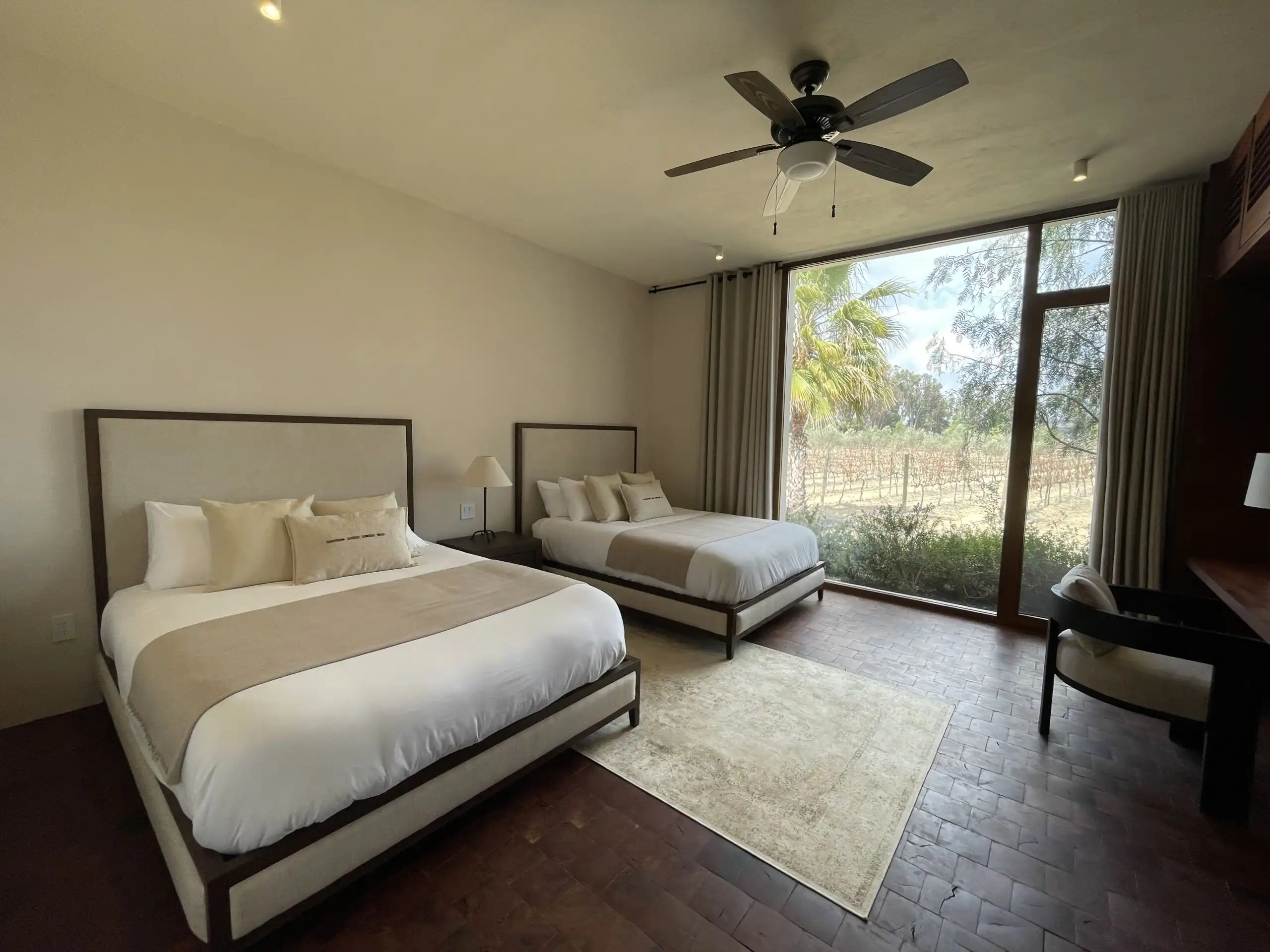 Luxury Vineyard Estate Bedroom in San Miguel de Allende Spacious bedroom with two large beds, modern decor, and large windows overlooking lush vineyards.